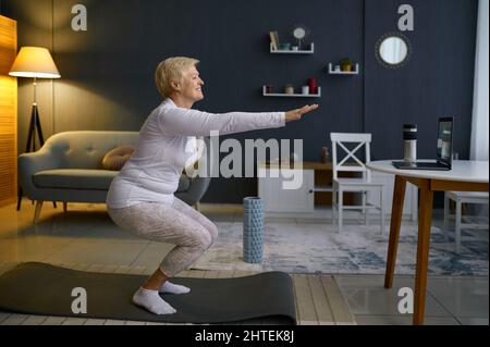 Ältere Frau macht Kniebeugen zu Hause trainieren Stockfoto