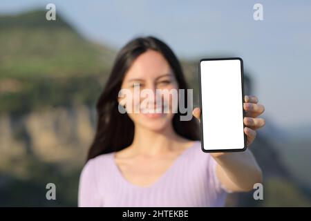 Vorderansicht Porträt einer glücklichen asiatischen Frau zeigt leeren Smartphone-Bildschirm im Freien in der Natur Stockfoto