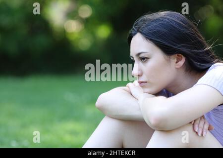 Traurige asiatische Frau, die sich beschwert, als sie allein in einem Park saß und wegschaute Stockfoto