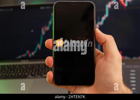 Bitcoin BTC App der Kryptowährung Aktienmarktanalyse auf dem Bildschirm des Mobiltelefons in Menschenhand und wachsenden Charts Trading-Daten im Hintergrund, Februar 2022, San Francisco, USA. Stockfoto
