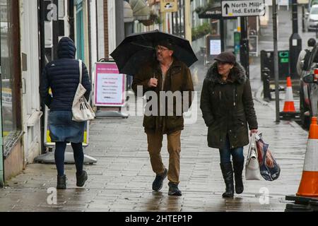 Bridport, Dorset, Großbritannien. 28.. Februar 2022. Wetter in Großbritannien. Bei dem starken Regen in Bridport in Dorset, an einem nassen Nachmittag am letzten Tag des meteorologischen Winters, halten sich die Käufer unter Regenschirmen auf dem Bürgersteig zurück. Bildnachweis: Graham Hunt/Alamy Live News Stockfoto