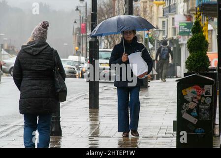 Bridport, Dorset, Großbritannien. 28.. Februar 2022. Wetter in Großbritannien. Eine Einkäuferin untersteht einem Regenschirm, während sie an einem nassen Nachmittag am letzten Tag des meteorologischen Winters in Bridport in Dorset durch den Straßenbelag geht. Bildnachweis: Graham Hunt/Alamy Live News Stockfoto