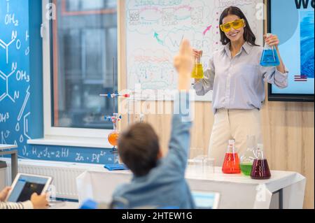 Lehrer mit Flaschen fragen und Schüler mit erhobener Hand Stockfoto