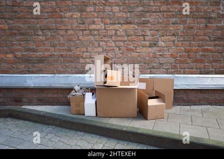 Stapel von gebrauchten Pappkartons werden auf dem Bürgersteig vor der alten Ziegelwand-Fassade gelassen. Stockfoto