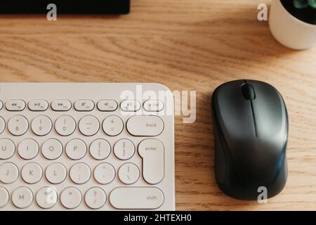 Draufsicht auf ein Büro mit einem weißen Keyboardtisch und einer schwarzen Maus auf einem Holztisch Stockfoto