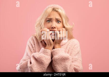 Angst junge Dame beißen Nägel vor Sorge, mit emotionalem Stress, Reaktion auf gruselige Nachrichten, rosa Studio-Hintergrund Stockfoto