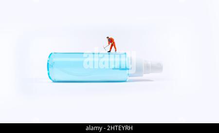 Figur eines Technikers, der auf einer Alkoholsprühflasche steht. Covid-19-Konzept. Stockfoto