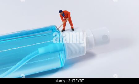 Figur eines Technikers, der auf einer Alkoholsprühflasche steht. Covid-19-Konzept. Stockfoto