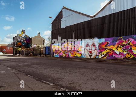 Lebendige Street Art ziert eine Mauer in Digbeth, Birmingham. An der Straßenecke steht Dead Wax, eine beliebte Bar und Veranstaltungsort für Live-Musik. Stockfoto