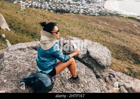 Eine Wanderin, die sich während der Wanderung auf einem Stein mit Thermoskannen entspannt Stockfoto
