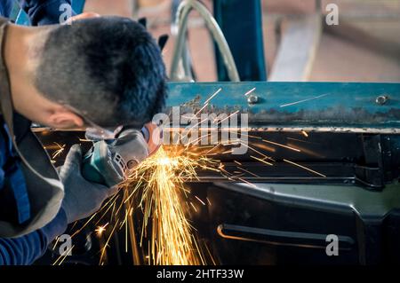 Junger Mann mechanische Arbeiter Reparatur einer alten Oldtimer-Karosserie In der chaotischen Garage - Sicherheit bei der Arbeit mit Schutz tragen Stockfoto