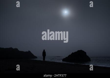 Silhouette einer Person, die an nebligen Tagen am Rande des Strandes steht Stockfoto