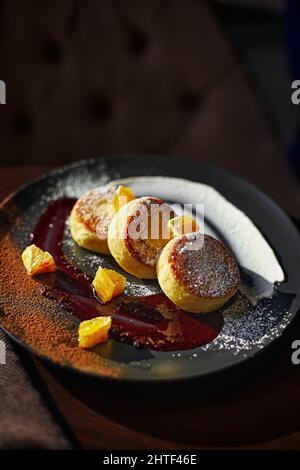 Käsekuchen oder Quark-Pfannkuchen mit Schokoladensauce und Orange auf einem Keramikplatte. Stockfoto