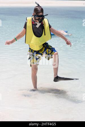 Kleiner Junge, der mit Schnorchelausrüstung in Flossen im seichten Wasser läuft