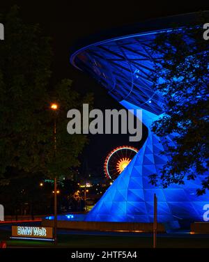 Die BMW Welt München als Teil der BMW Zentrale in München mit einem Riesenrad im Hintergrund blau beleuchtet Stockfoto