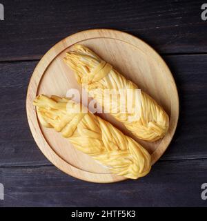 Geräuchertes, geflochtenes Käsestück auf einem dunklen Holztisch Stockfoto