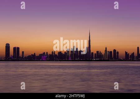 Skyline von Dubai Downtown nach Sonnenuntergang während der goldenen Stunde mit purpurem Himmel und Dubai Creek Canal, Langzeitbelichtung. Stockfoto