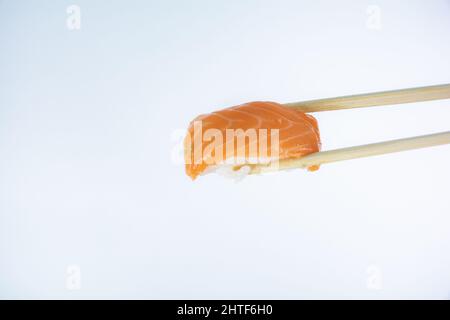 Nahaufnahme von Lachs-Nigiri, gehalten mit Bambusstäbchen isoliert auf weißem Hintergrund Stockfoto