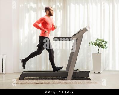 Ganzkörperaufnahme eines bärtigen Mannes in Sportbekleidung, der zu Hause auf einem Laufband läuft Stockfoto