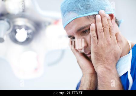 Wie erzähle ich es der Familie. Nahaufnahme ein Arzt, der etwas verzweifelt aussieht und seinen Kopf in den Händen hält. Stockfoto