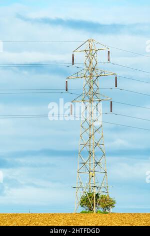 Strompylon des britischen National Grid, der von Sonnenlicht an einem flachen Horizont vor einem weißen und blauen Himmel beleuchtet wird. Stockfoto