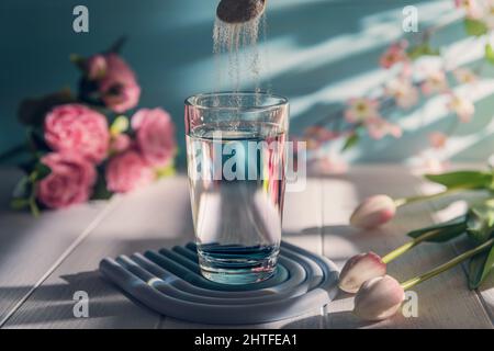 Kollagenpulver wird mit einem Löffel in ein Glas Wasser gegeben Stockfoto