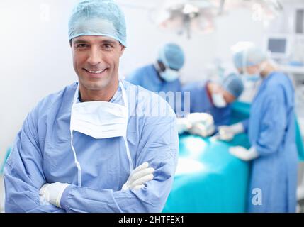Ich habe ein Team von chirurgischen Experten hinter mir. Porträt eines glücklichen, selbstbewussten und professionellen Arztes mit seinem Team von chirurgischen Experten hinter ihm. Stockfoto