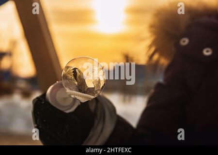 Ein Mädchen hält eine Seifenblase mit schönen Frostmustern in den Strahlen der Sonne Stockfoto