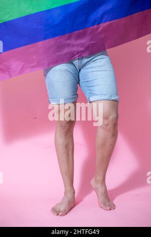 Mittelteil eines jungen Mexikaners, der mit LGBT-Flagge vor einem rosa Hintergrund posiert Stockfoto