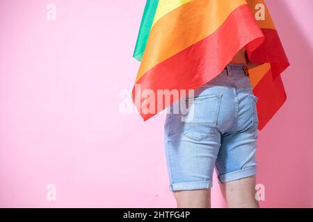 Mittelteil eines jungen Mexikaners, der mit LGBT-Flagge vor einem rosa Hintergrund posiert Stockfoto