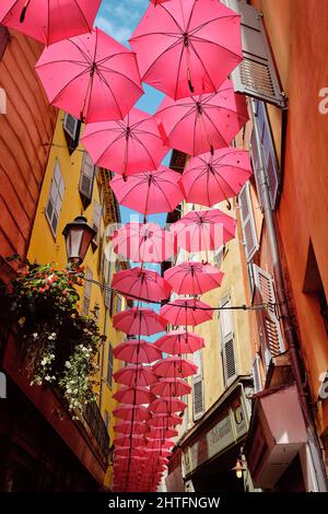 Eine vertikale Aufnahme von rosa Regenschirmen, die über einer Straße in Grasse, Frankreich, hängen Stockfoto