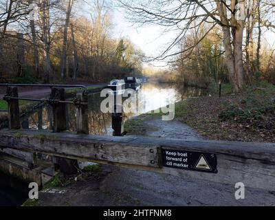 Boote, die im Winter auf einem Kanal mit einem Schleusentor im Vordergrund im Cassiobury Park, Watford, Hertfordshire, festgemacht wurden. Stockfoto