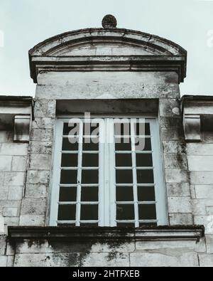 Vertikale Graustufenaufnahme eines alten Gebäudes mit einem Holzfenster Stockfoto