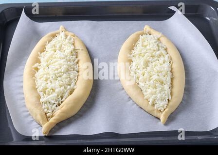 Prozess des Kochens georgischen khachapuri mit Käse, Kuchen in Form eines Bootes werden mit Käse gefüllt und auf einem Backblech gelegt, Schritt für Schritt ins Stockfoto