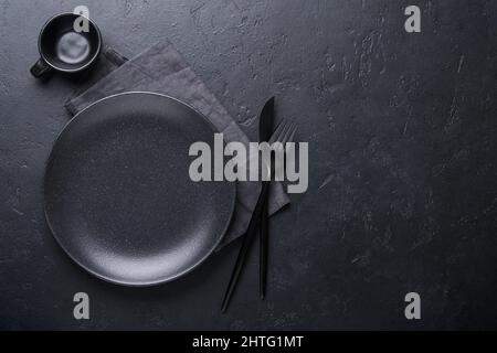 Schwarzer Löffel, Gabel, Messer und leere schwarze Platte reinigen. Set aus stilvollem schwarz-goldenem Besteck auf schwarzem Hintergrund. Modisches und luxuriöses Essen. Oben vi Stockfoto