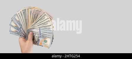 Banner mit einer Hand, die 100-Dollar-Scheine auf grauem Hintergrund hält. Amerikanisches Geld. Für Text platzieren. Hochwertige Fotos Stockfoto