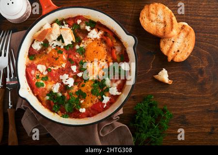 Shakshuka. Hausgemachte Spiegeleier in Tomatensoße, Olivenöl, Paprika, Zwiebel und Knoblauch in einer eisernen Pfanne auf altem Holzhintergrund pochiert. Traditi Stockfoto