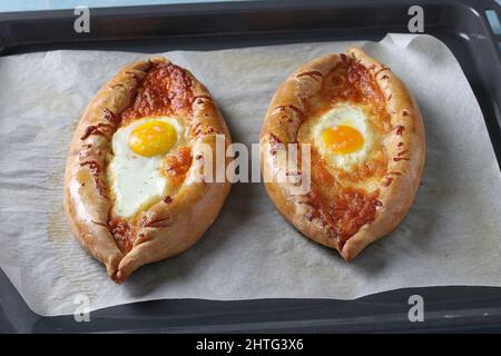 Khachapuri in Adjarian mit Suluguni-Käse und Ei, offene Torten in Form eines Bootes, auf Backblech gebacken, traditionelle georgische Küche Stockfoto