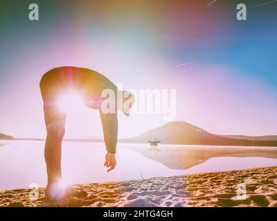 Sportmann Stretching biegen Sie zurück am Strand. Läufer beim Training am See. Abstraktes Licht, farbenfrohe Lichtreflexe. Stockfoto