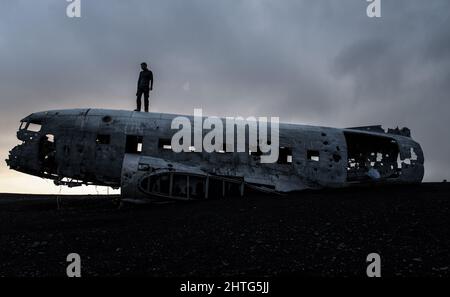 Silhouette Aufnahme eines Mannes, der auf einem alten verlassenen, zerbrochenen Flugzeug in Island steht Stockfoto