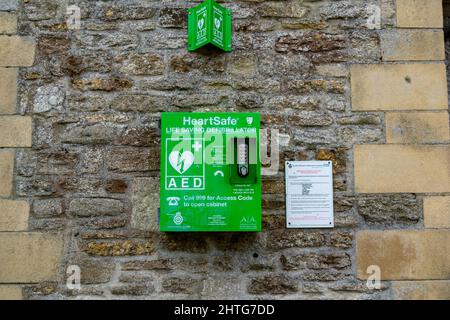 Lacock, UK-Sept 2021: Grüner Defibrillatorschrank von vorne gesehen, an der Gebäudewand befestigt, damit jeder ihn im Notfall, im Leben, benutzen kann Stockfoto