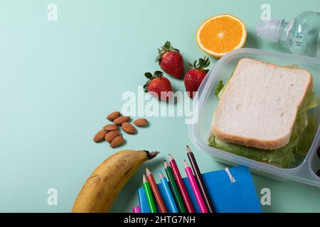 Sandwich in Lunchbox mit Früchten, Mandeln und Farbstiften mit Büchern auf grünem Hintergrund Stockfoto