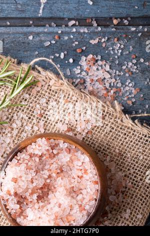 Nahaufnahme von himalaya-rosa Steinsalz in Holzschüssel mit Rosmarin auf Jute-Stoff über dem Tisch Stockfoto