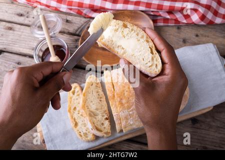 Nahaufnahme eines afroamerikanischen Mannes, der die Hände mit Butter auf die Brotscheibe auftauchte Stockfoto