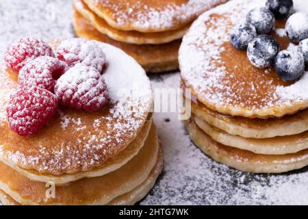 Nahaufnahme von Puderzucker über gestapelten Pfannkuchen mit blauen Beeren und Himbeeren Stockfoto