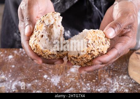 Nahaufnahme eines afroamerikanischen männlichen Bäckers, der Brot auf den Tisch brach Stockfoto