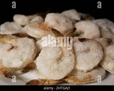Gefrorene Garnelen auf einem weißen Teller, schwarzer Hintergrund Stockfoto