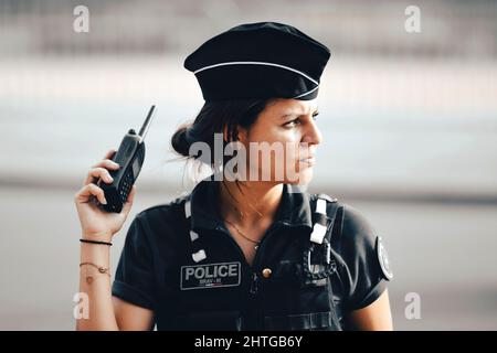 Eine diensthabende französische Polizeibeamtin, die ein Funkgerät mit Funksprechanlage in der Hand hält, sorgt für die Sicherheit der Bürger in einer Pariser Straße. Stockfoto