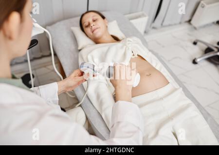 Nahaufnahme einer Ärztin, die Gel auf den Ultraschallaufnehmer legt, während sie eine Schwangere in der Klinik untersucht, Platz kopieren Stockfoto