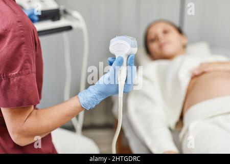 Nahaufnahme einer Ärztin, die den Ultraschallaufnehmer hält, während sie eine Schwangere in der Klinik untersucht, Platz kopieren Stockfoto